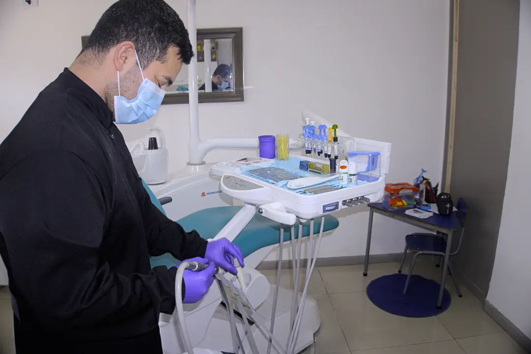 El doctor, con mascarilla, prepara el instrumental junto al sillón dental