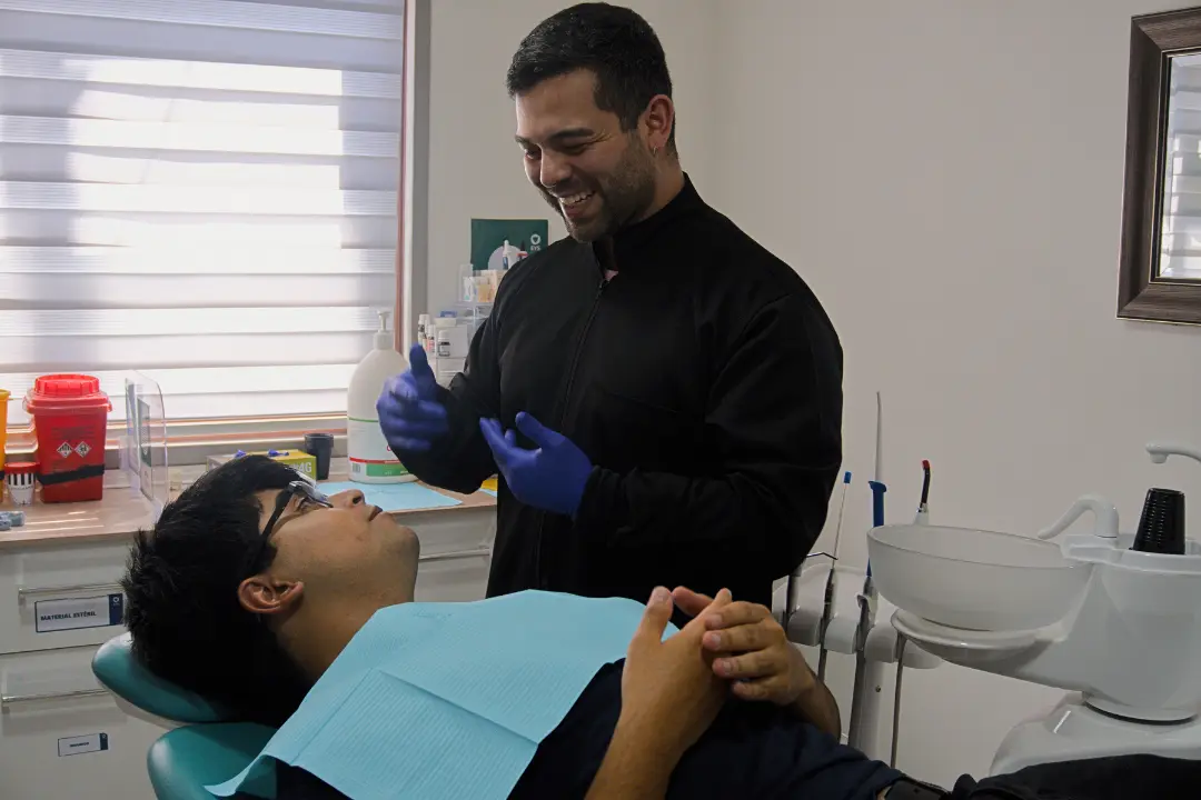 El doctor sonríe junto a un paciente recostado en el sillón dental