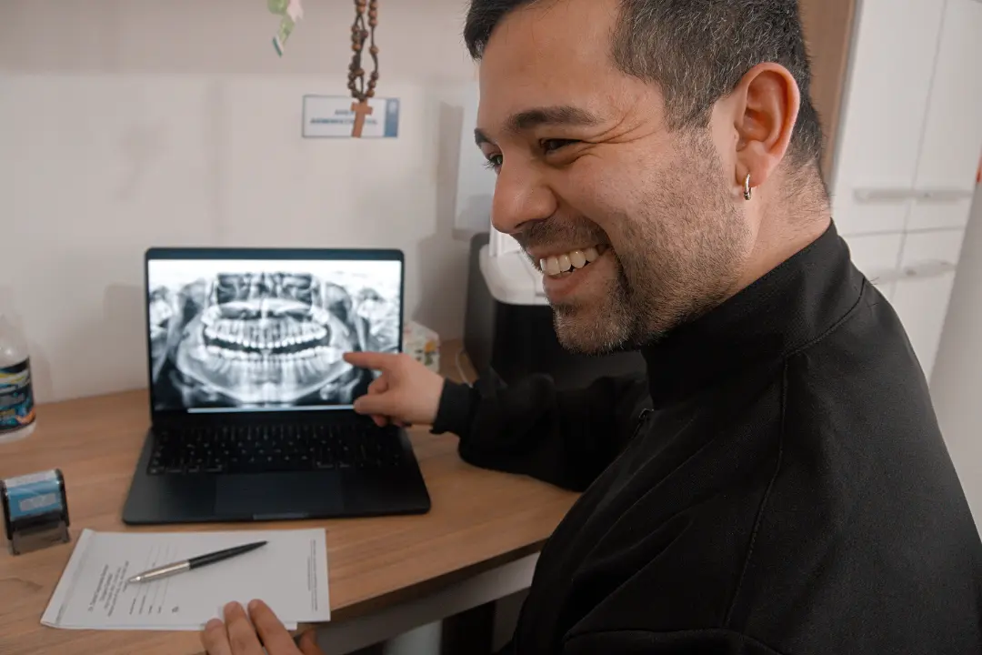 El doctor sonríe mientras señala una radiografía panorámica en su computador